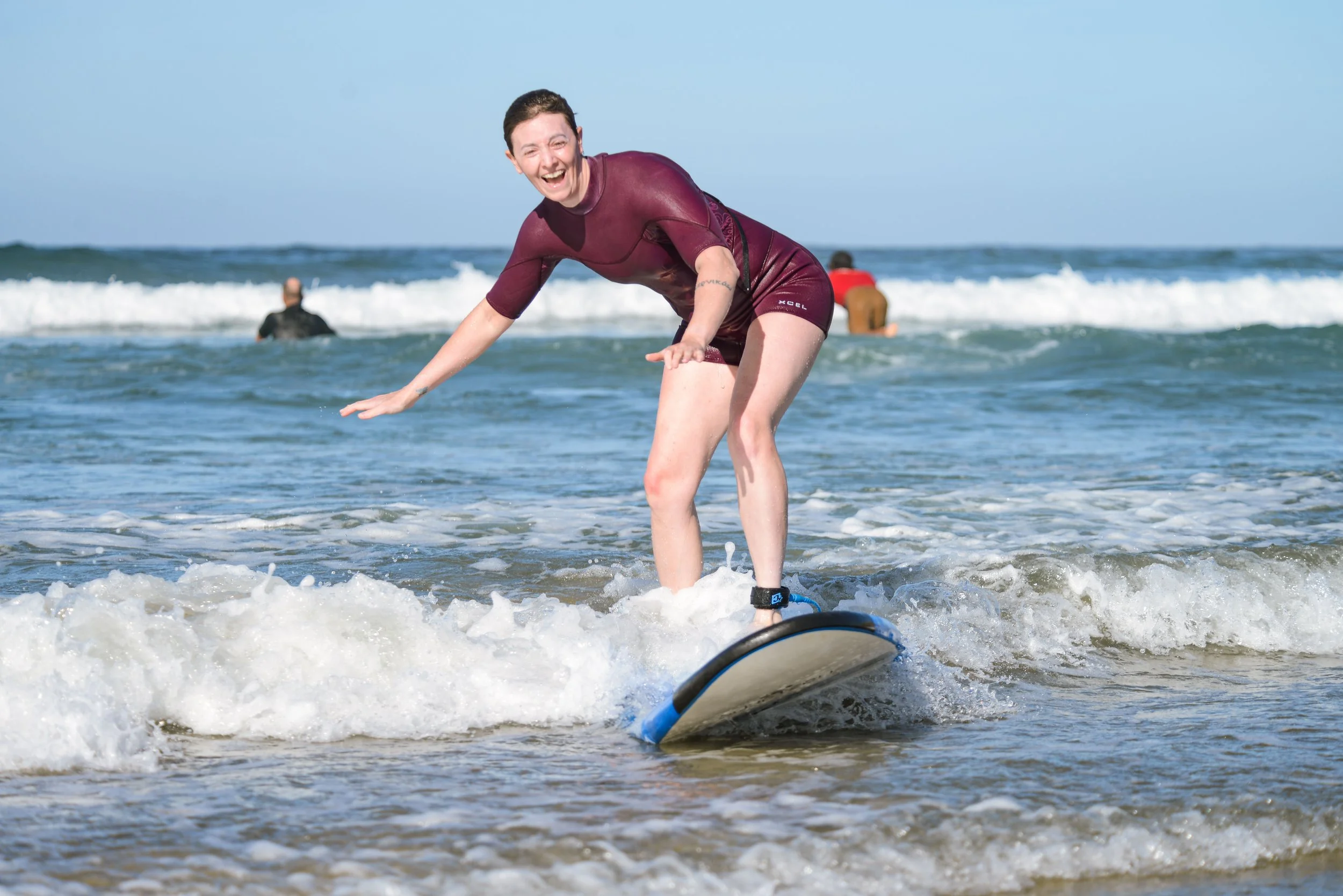 Woman smiling while balancing on a paddleboard in the ocean with two people in the background.