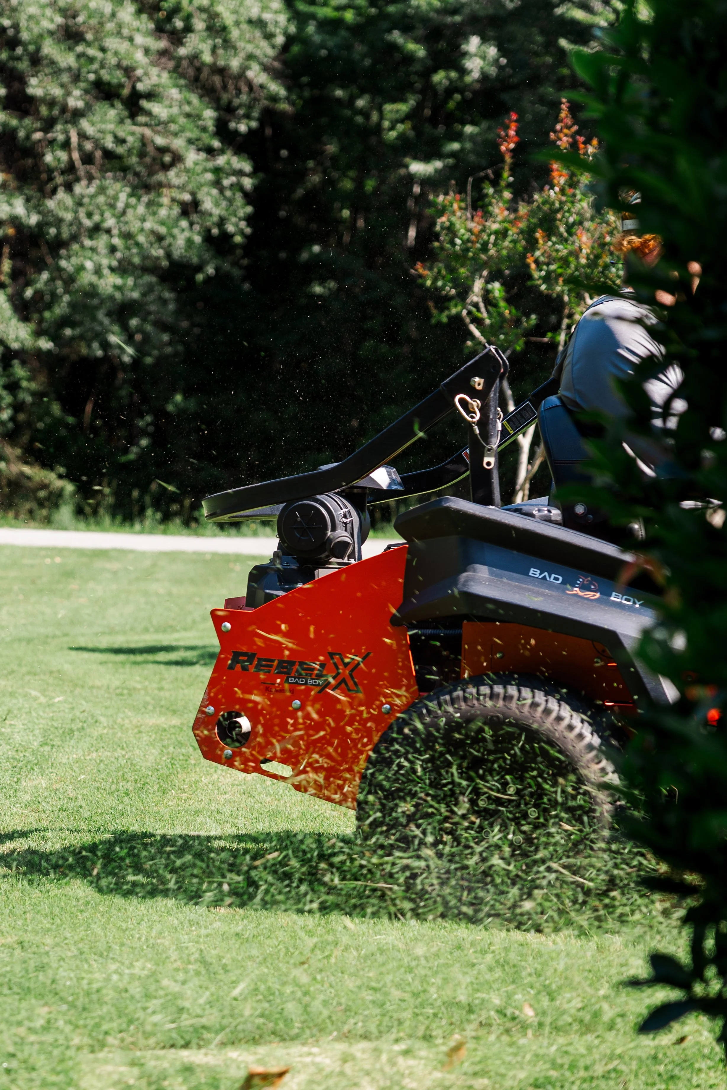 Revive Landscape Helena Alabama A person using a leaf blower to blow leaves on a lawn, partially obscured by trees and bushes.