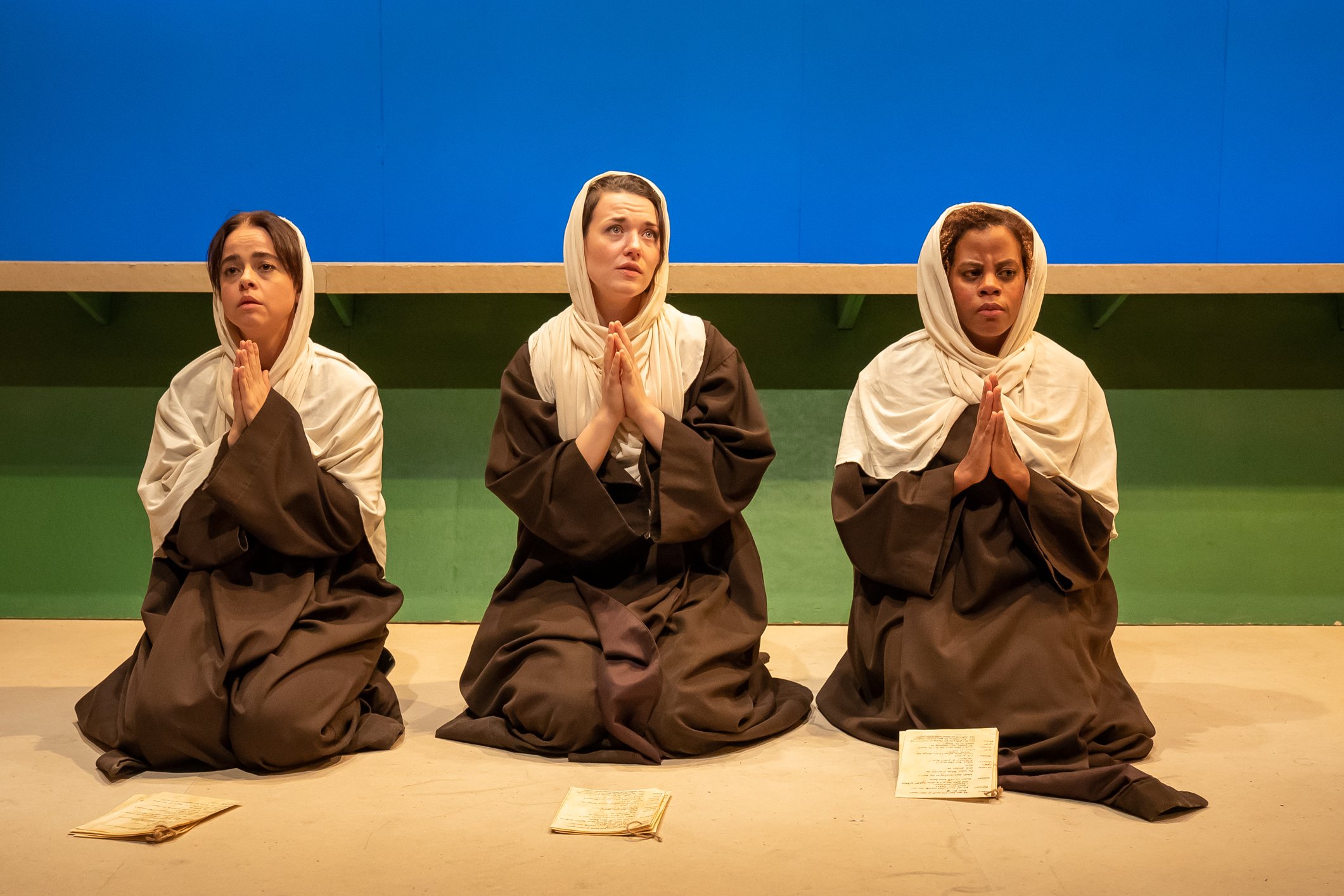 Three women dressed as nuns kneel on the ground, praying.