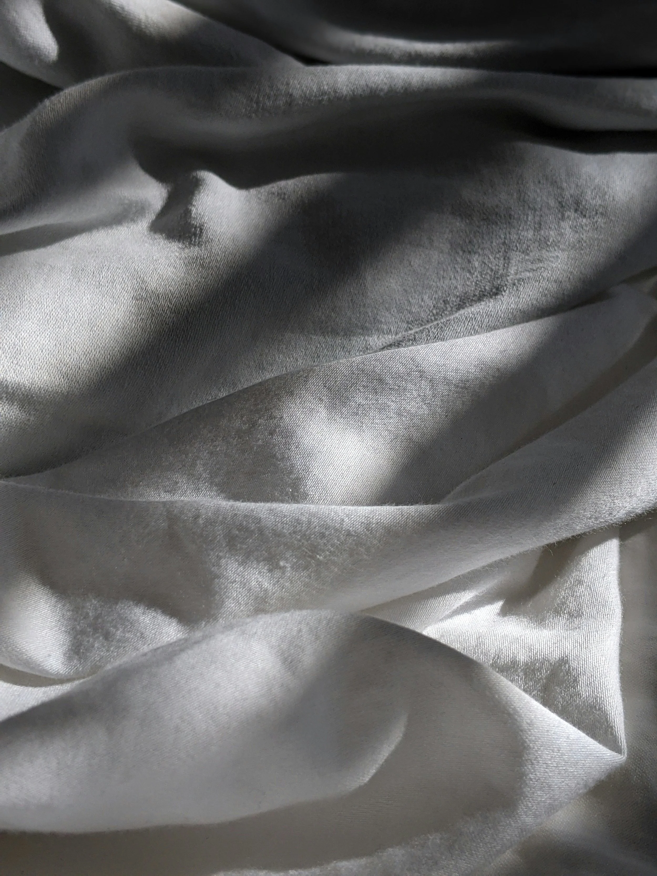 Close-up of smooth, shiny silver satin fabric with soft folds and creases.