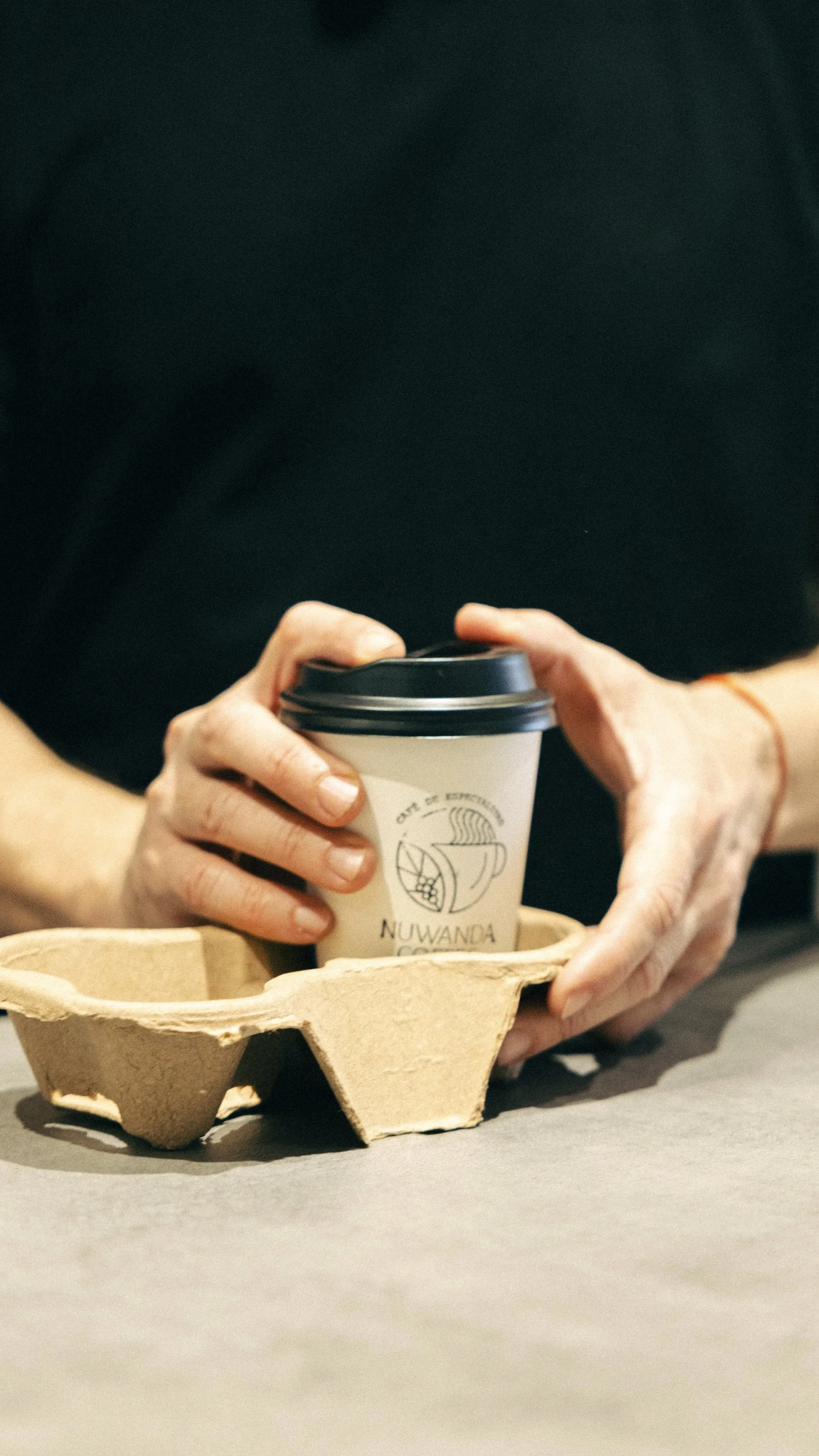 Person holding a take away coffee cup with a logo, placed on a cardboard tray.