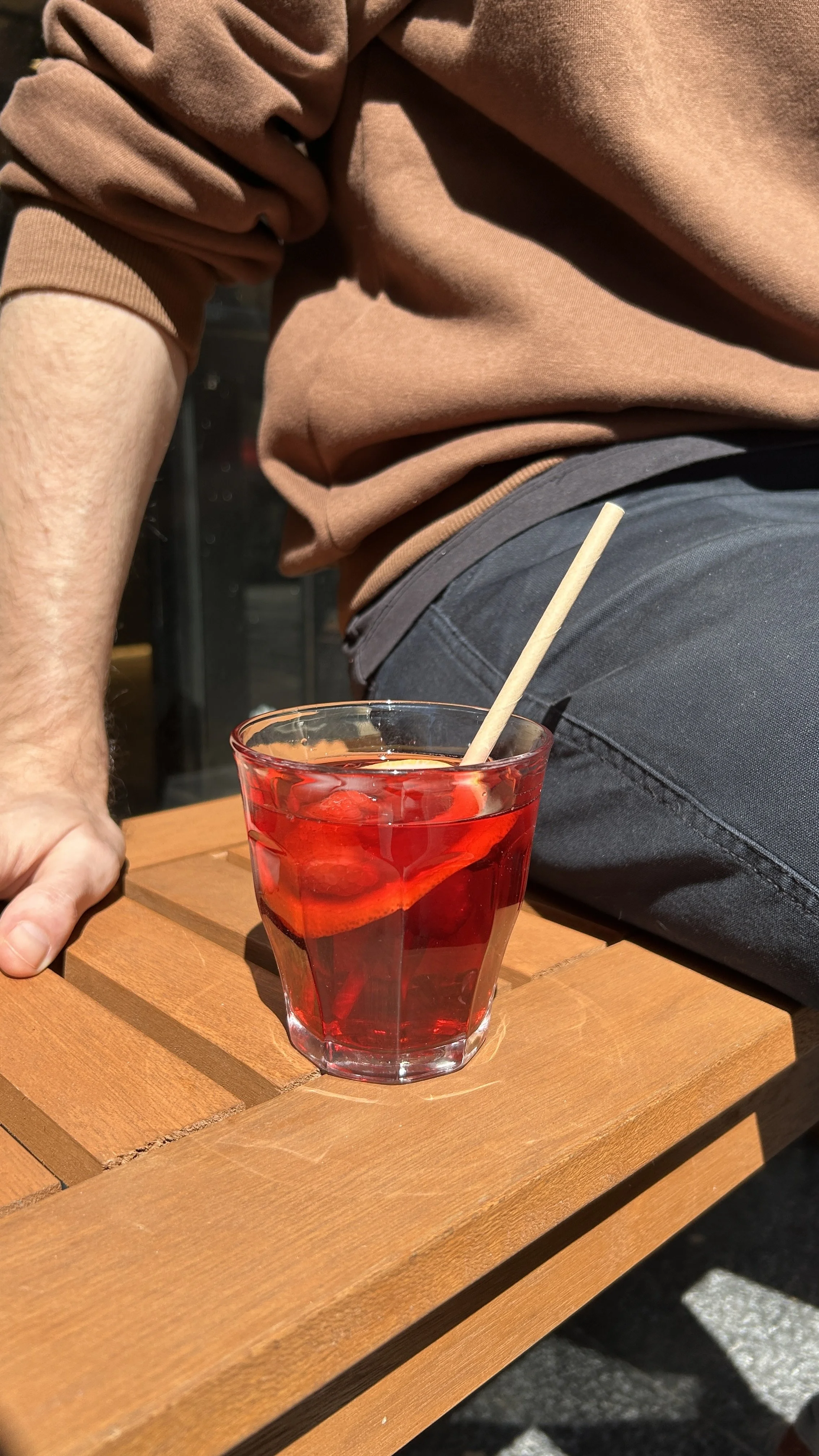 A glass of red drink, hibiscus lemon,  with ice and a straw on a wooden table.