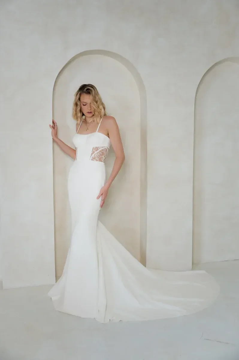 A woman in a white wedding dress standing in front of a wall with arched niches.