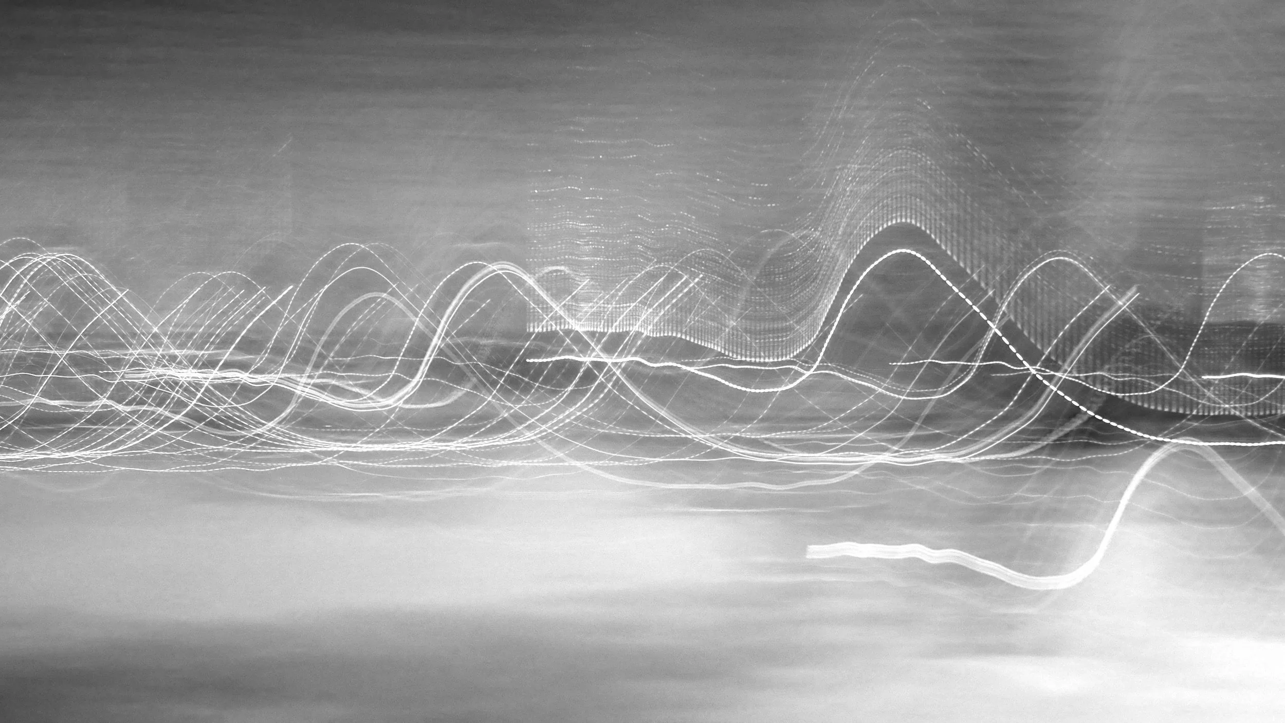 Black and white photo of light trails creating smooth, flowing lines across the image, resembling abstract wave patterns or data visualizations.