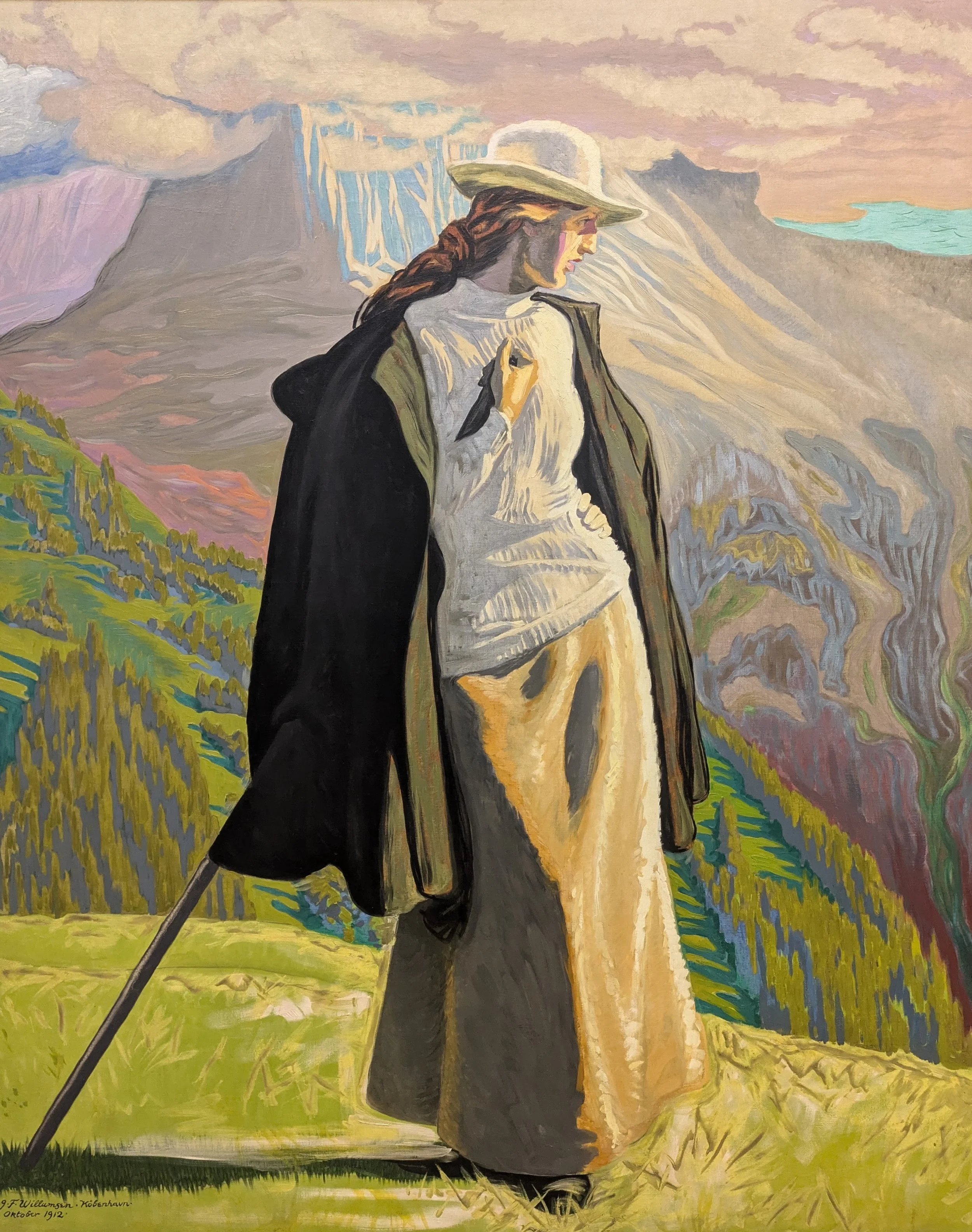 A woman with brown hair in a braid wearing a wide-brimmed hat, a dark coat, a light sweater, and pants, holding a walking stick, standing on green grass with mountains and a cloudy sky in the background, painted in an impressionist style.