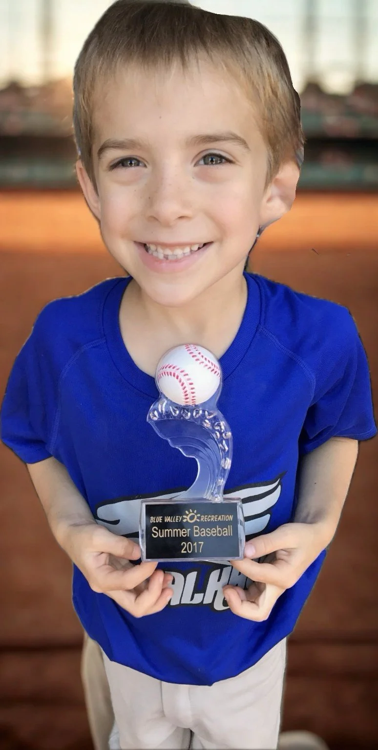 Leonardo smiling and holding a baseball trophy during summer baseball in 2017, wearing a blue shirt.