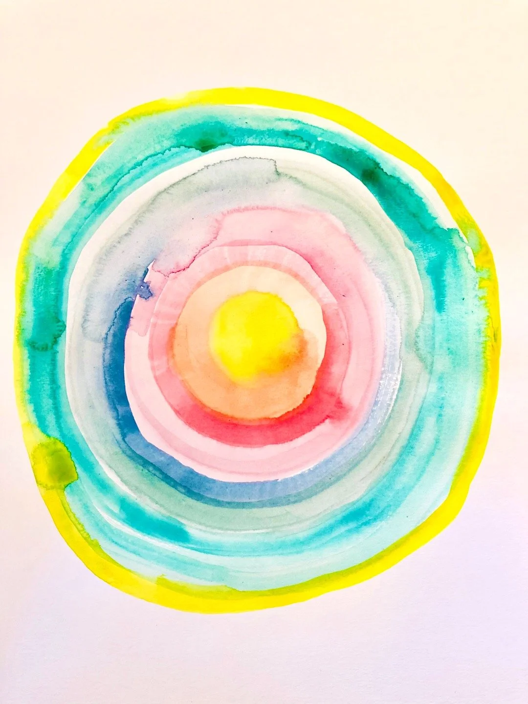 Watercolor painting of a softly colorful concentric circle pattern with lightly toned yellow, pink, blue, green, and white hues on paper.