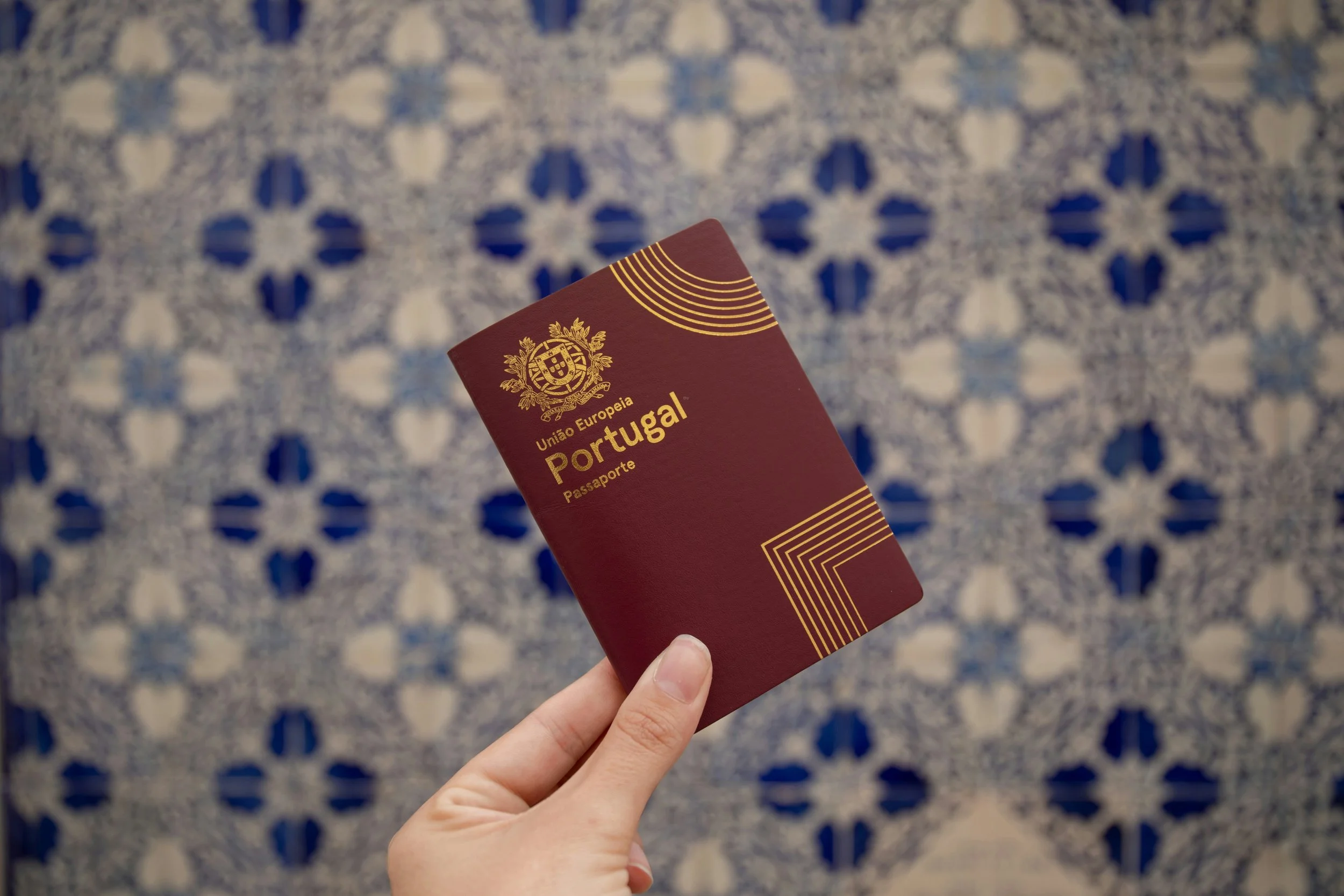 Person holding a Portuguese passport against a blue and white patterned background.