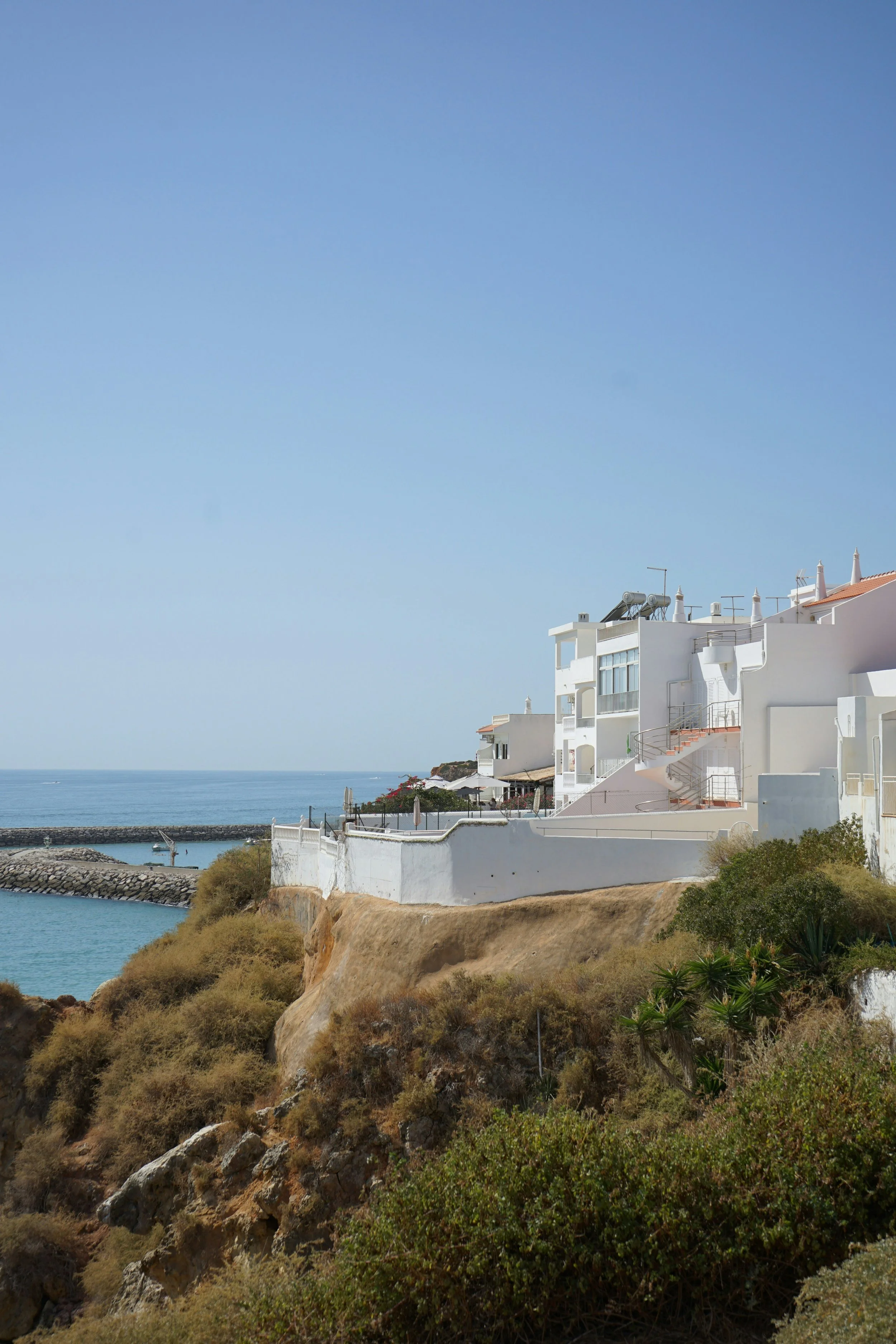 White modern buildings on a cliff overlooking the sea, with a clear blue sky overhead.