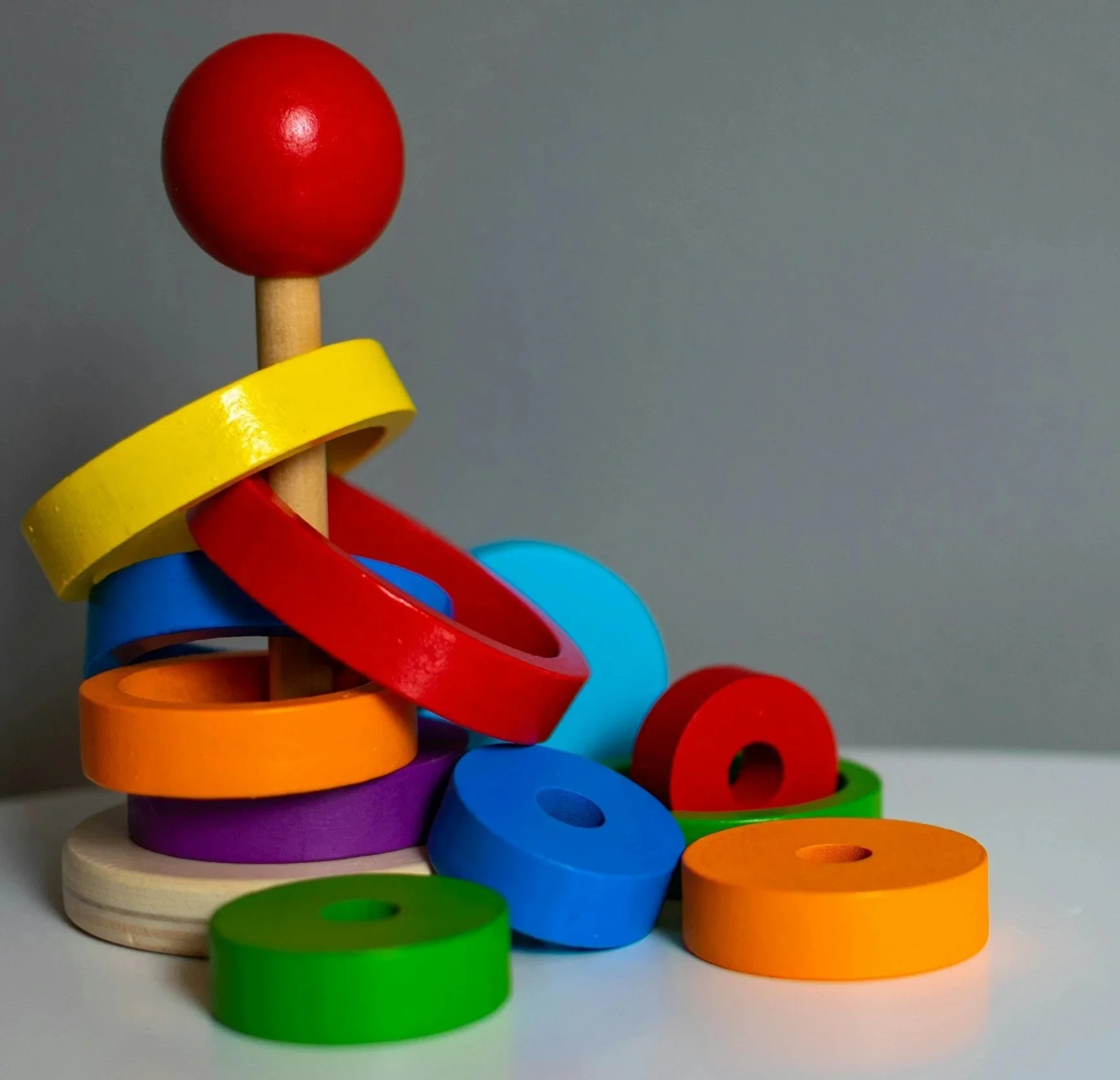 Colorful wooden stacking rings arranged in a tower with a red ball on top, on a gray background.