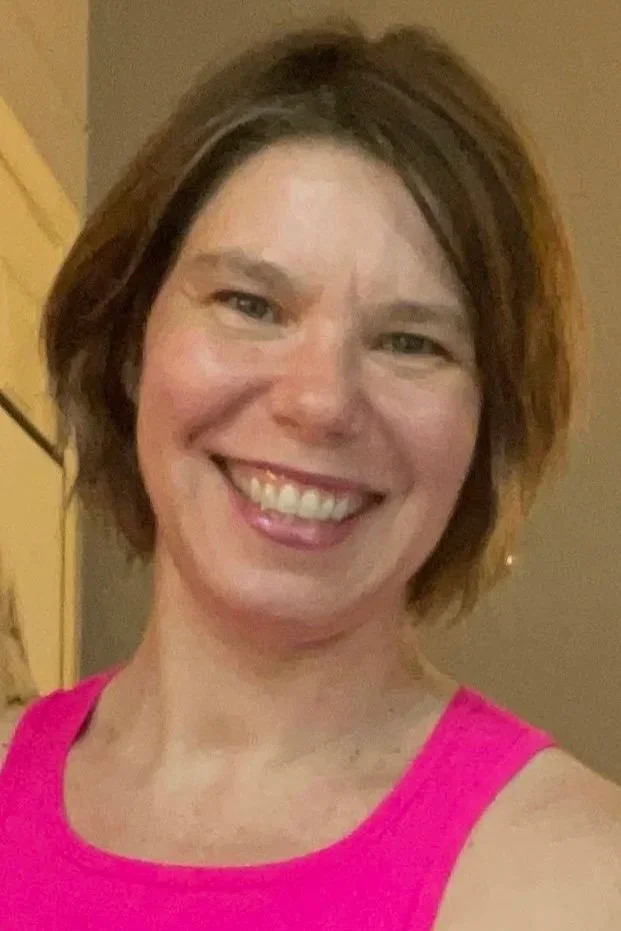 Smiling woman with short brown hair and light skin in a pink sleeveless top.