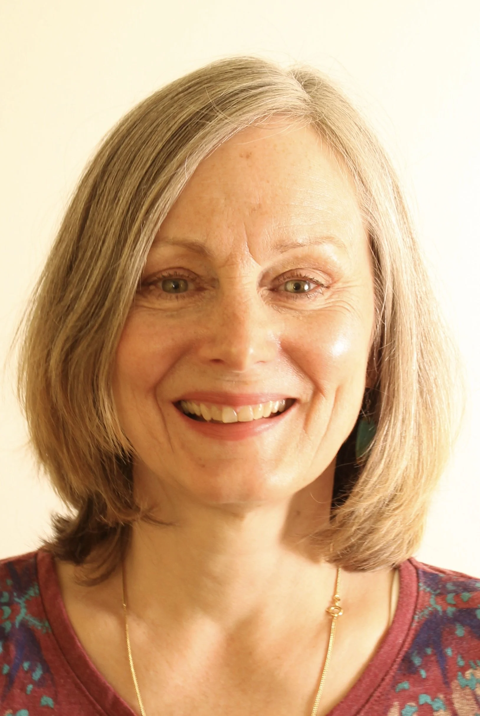 A smiling woman with blonde hair wearing a patterned top and a gold necklace.