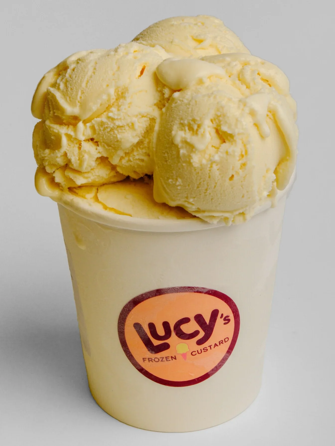 A cup of vanilla ice cream with chunks of vanilla bean on top, in a liquid cup with Lucy's Frozen Custard logo.