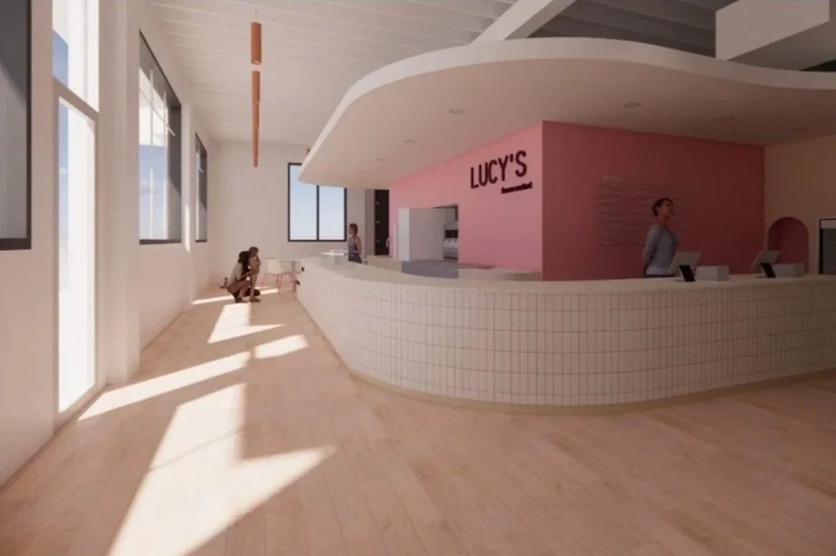 Interior of a modern lobby with a pink Lucy's restaurant counter, two women at the counter, one seated near a window, sunlight streaming in. Frozen Custard East Vancouver, BC