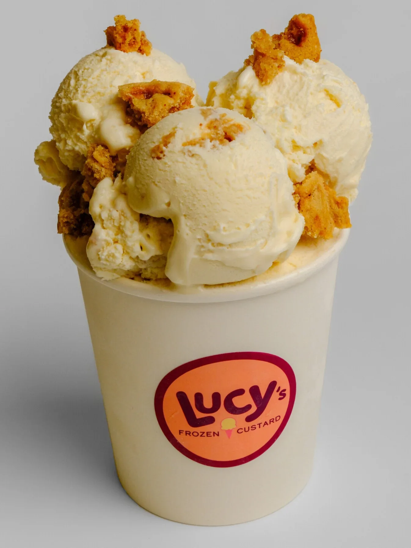 A cup of vanilla ice cream topped with cookies and white chocolate chunks, in a Lucy's Frozen Custard cup.