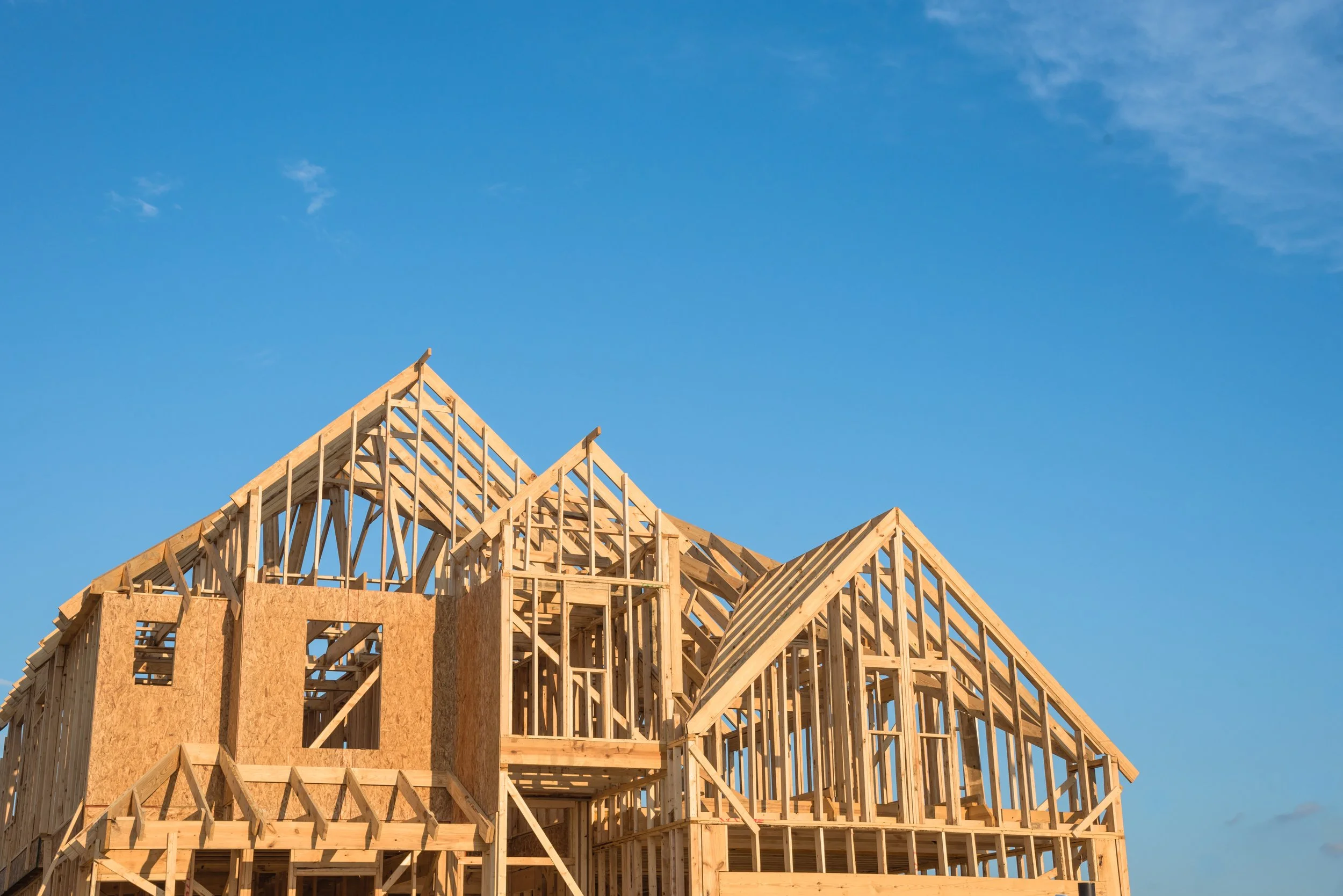 Wooden framework of a building under construction against a clear blue sky.