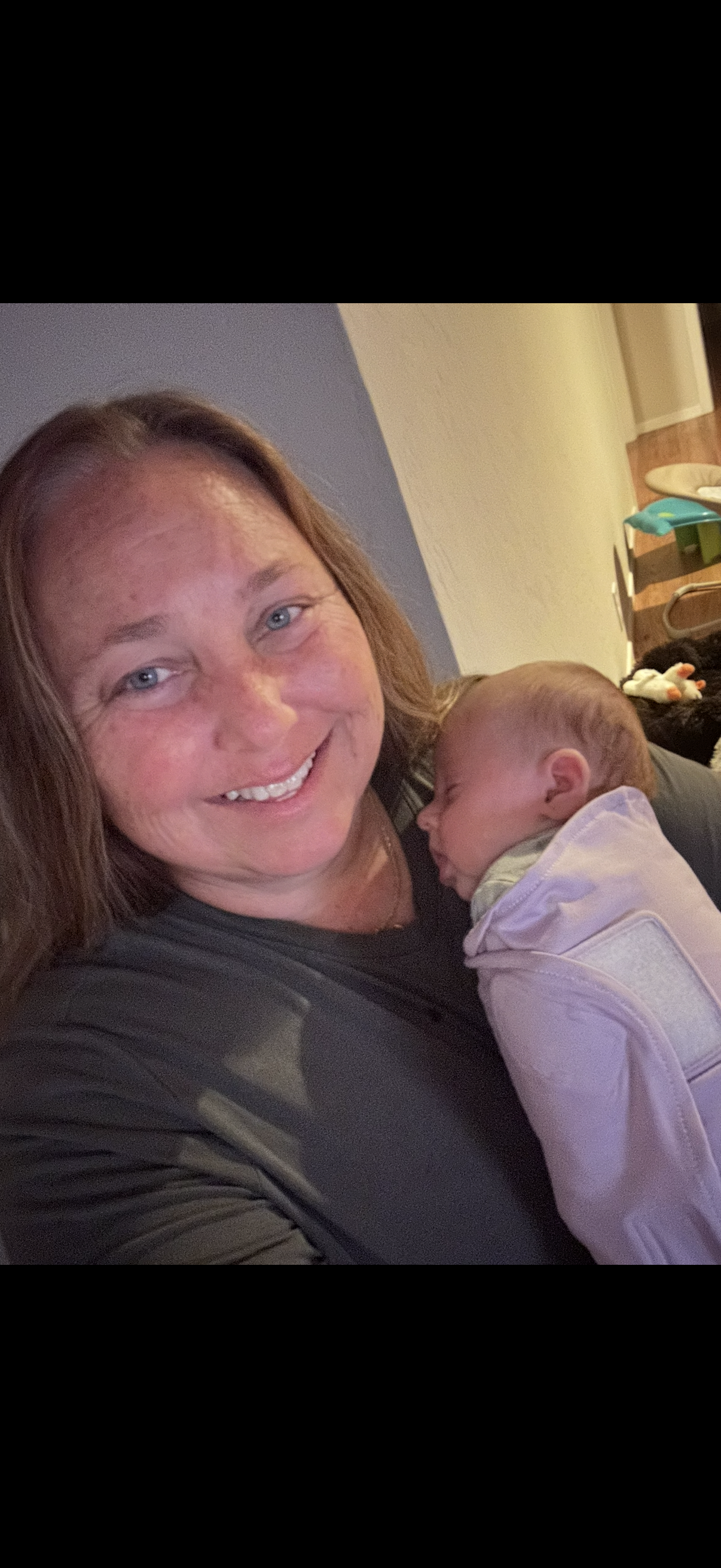 A woman with brown hair smiling and holding a sleeping baby with red hair and closed eyes.