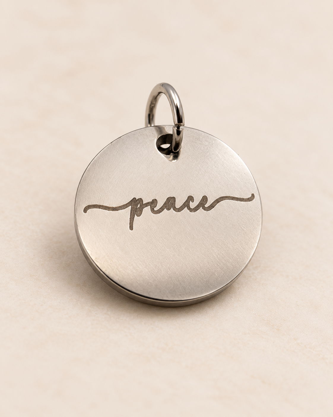 A round metal keychain with the word 'peace' engraved in cursive, attached to a small hook.