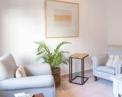 Living room with two white armchairs, a green potted plant, a wooden side table, and a framed art print on the wall