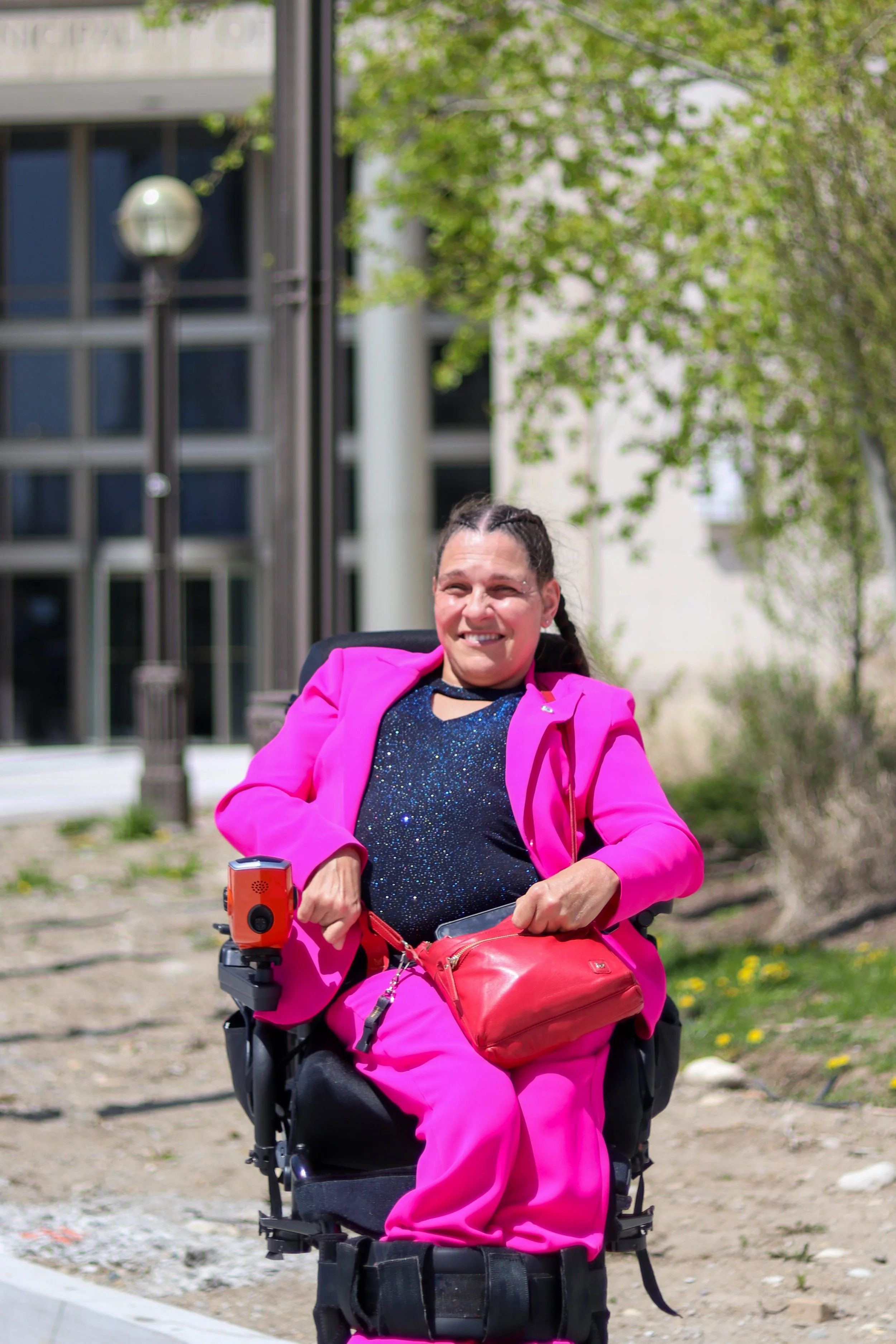 Regional Councillor Chantal Huinink sits in her wheelchair wearing a pink suit, in front of the regional council building