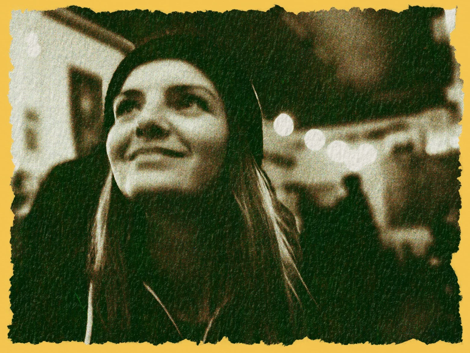 A woman with long hair and a confident smile, standing outdoors at night with blurry people and lights in the background.