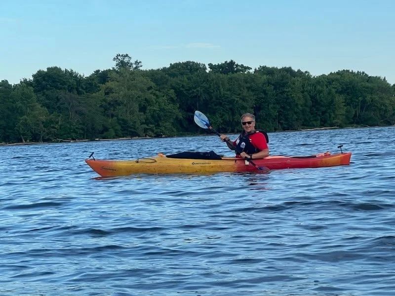 A man kayaking on a lake with a background of green trees and a clear sky.