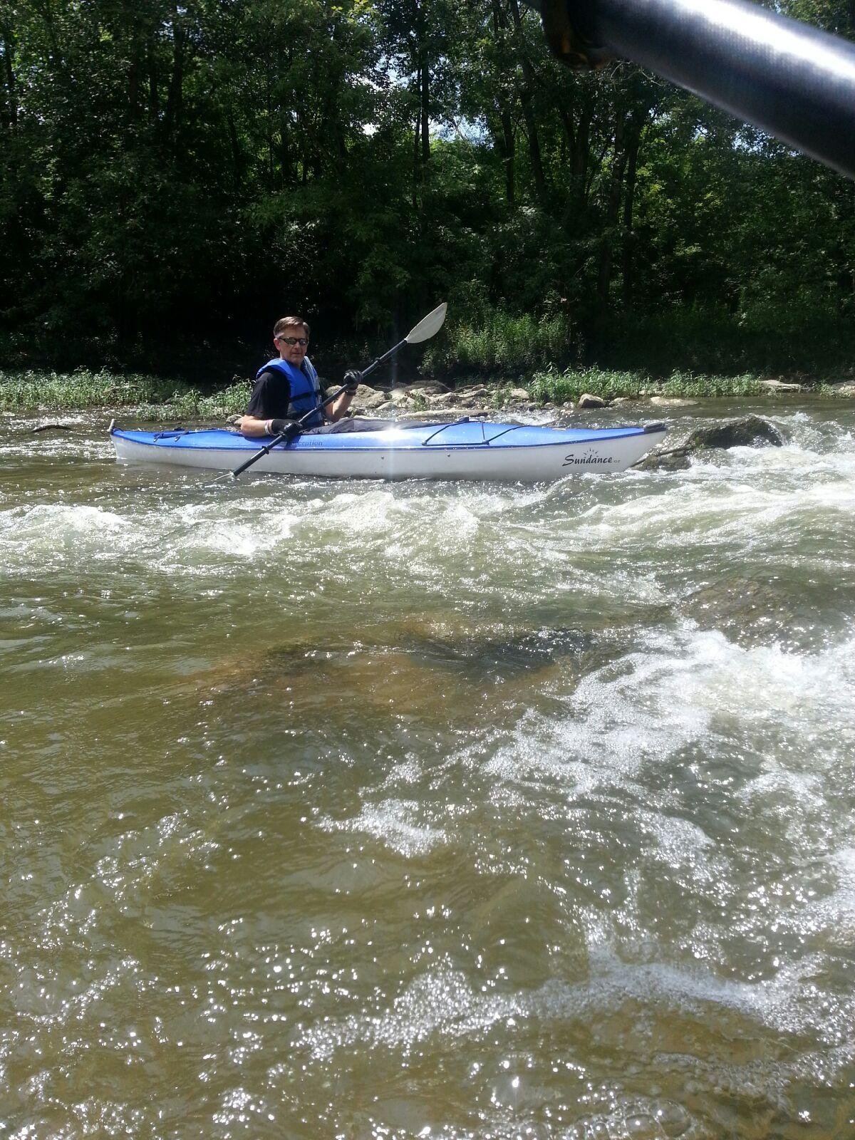 A person kayaking on a river surrounded by trees.