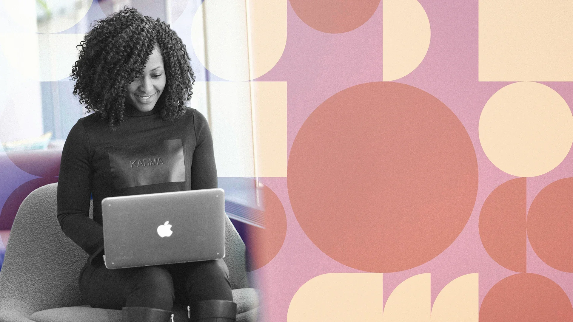 A woman with curly hair smiling while working on a laptop in an office setting.
