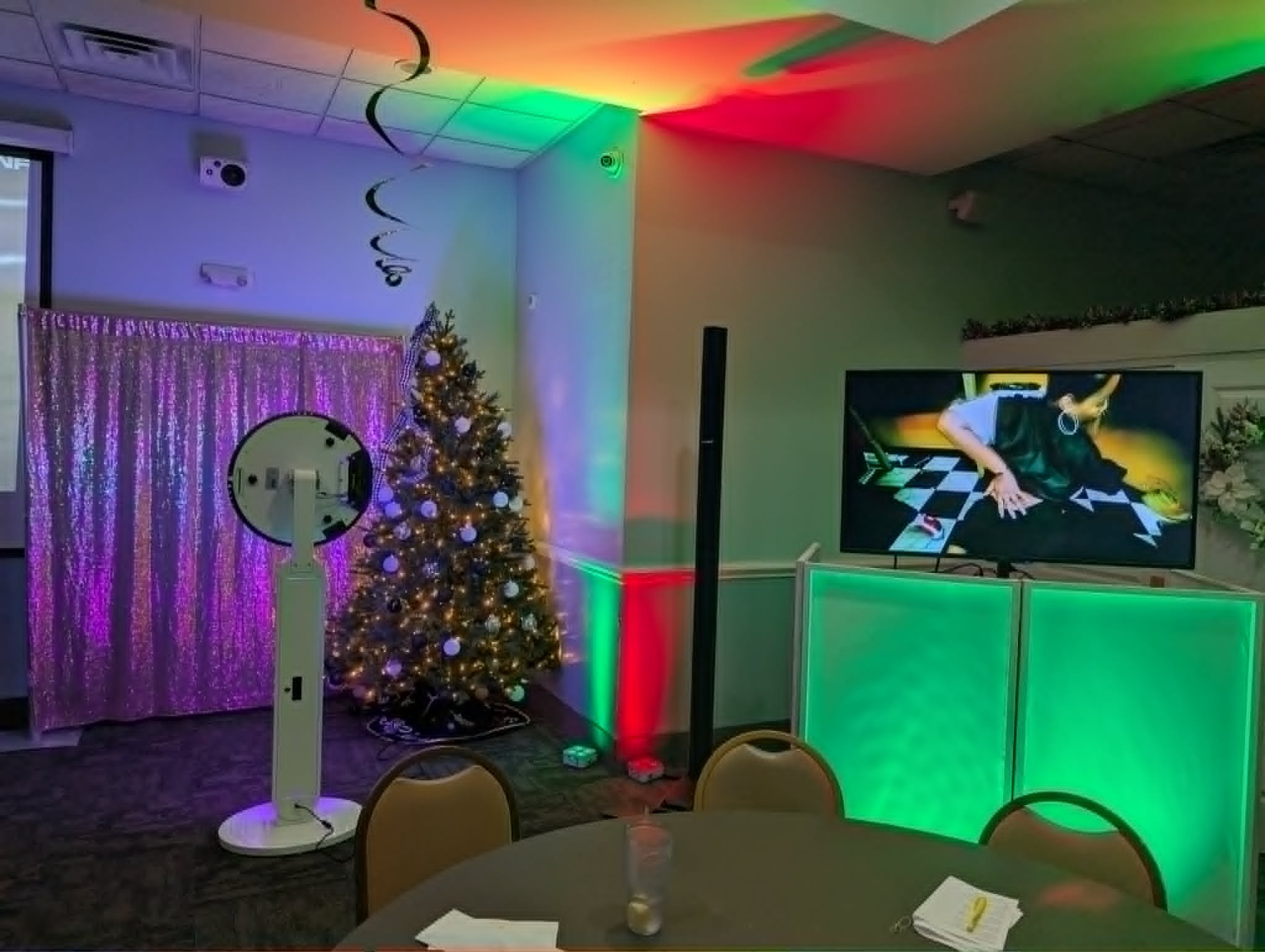 Interior decorated for a celebration with colorful lights, a Christmas tree with ornaments, a pink curtain, a mirror, a speaker, and a television showing a person in a white shirt and apron.