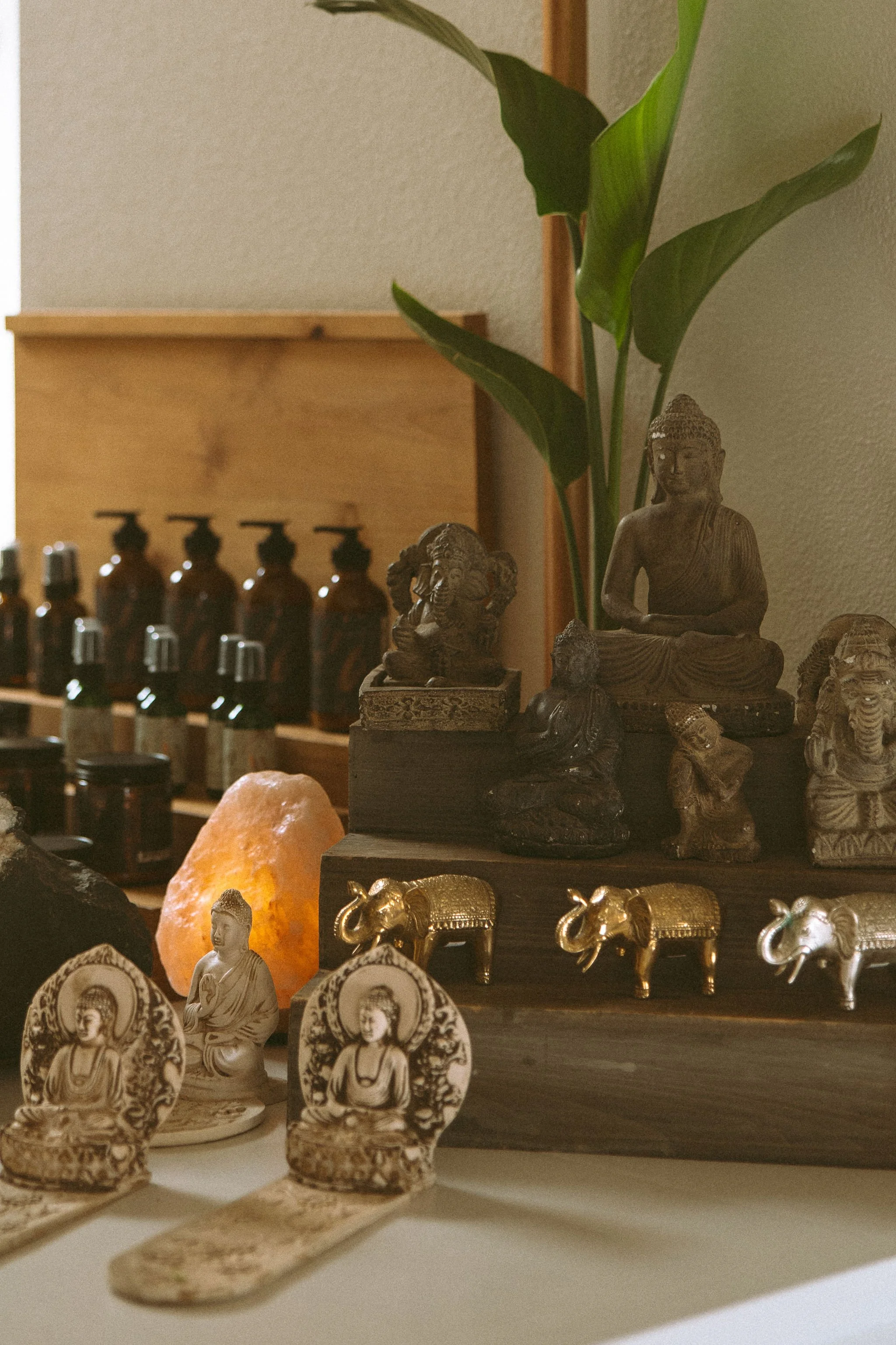 Display of various small Buddha and elephant figurines, a salt lamp, and cannabis leaf-shaped objects on shelves.