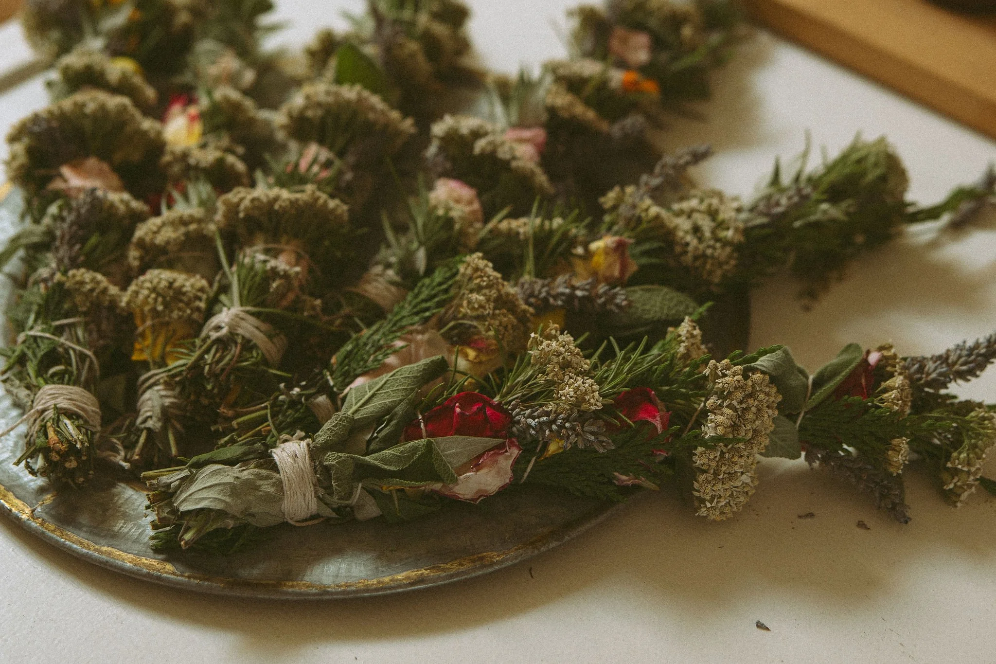 Dried herb bundles and flower wreaths on a silver tray with a gold edge, placed on a white surface.