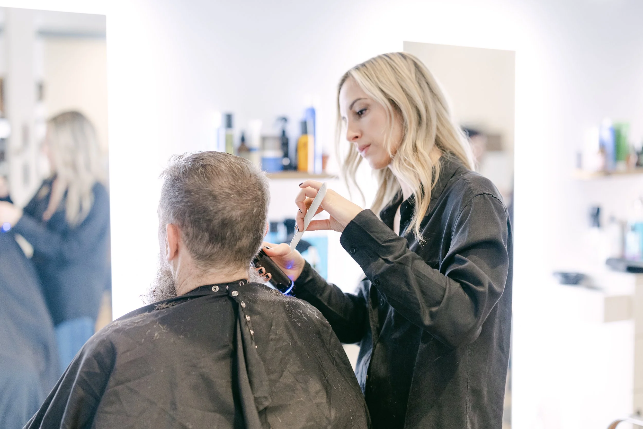 A female hairstylist cuts a male client's hair in a salon.