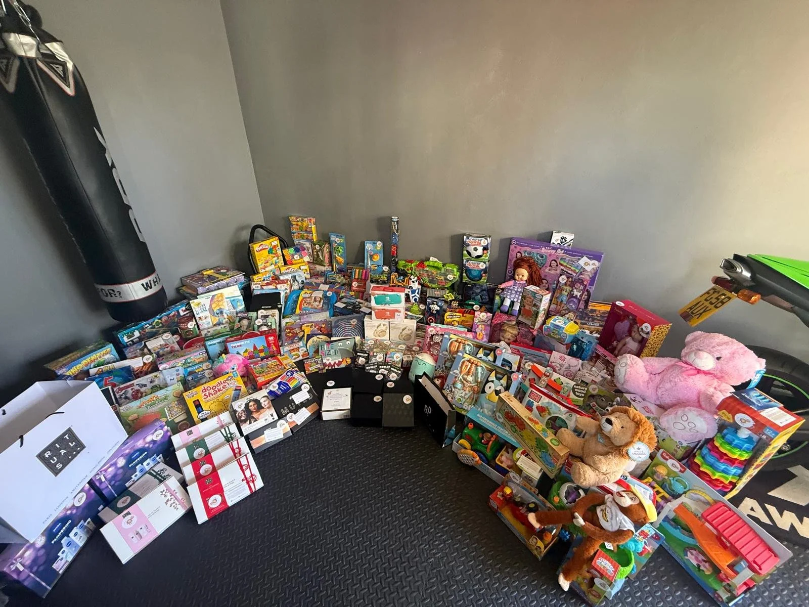 A large collection of toys arranged against a wall, including stuffed animals, dolls, board games, and various boxed playsets.
