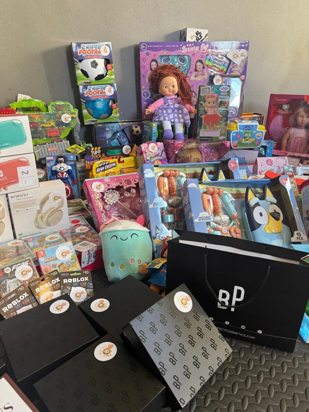 A table filled with various toys, gift boxes, and shopping bags, including dolls, action figures, and accessories.