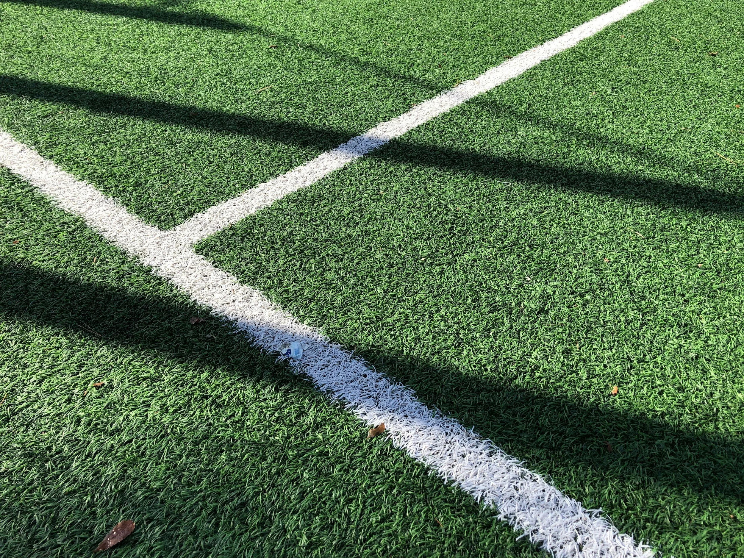 Close-up of a green artificial turf field with a white boundary line and cast shadows.