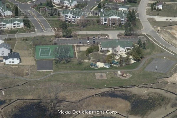 Aerial view of a residential neighborhood with a tennis court, swimming pool, playground, and parking lot.