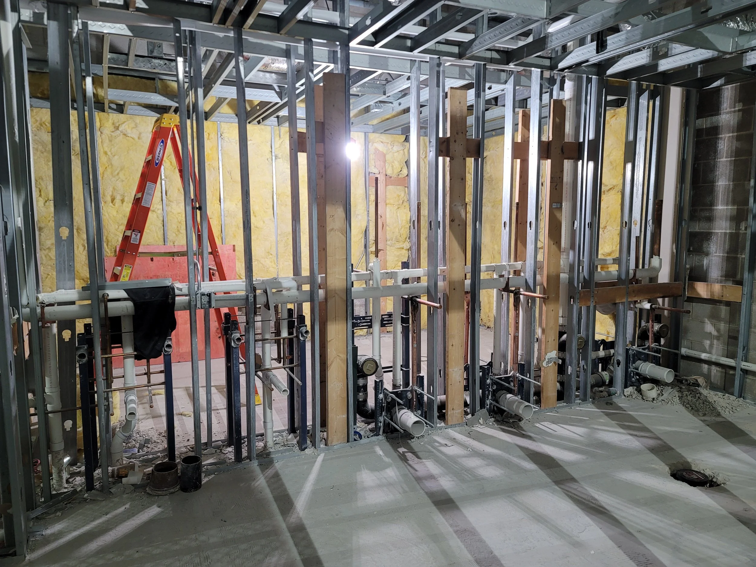 Construction site with metal framing, wooden studs, and plumbing pipes in an unfinished room.