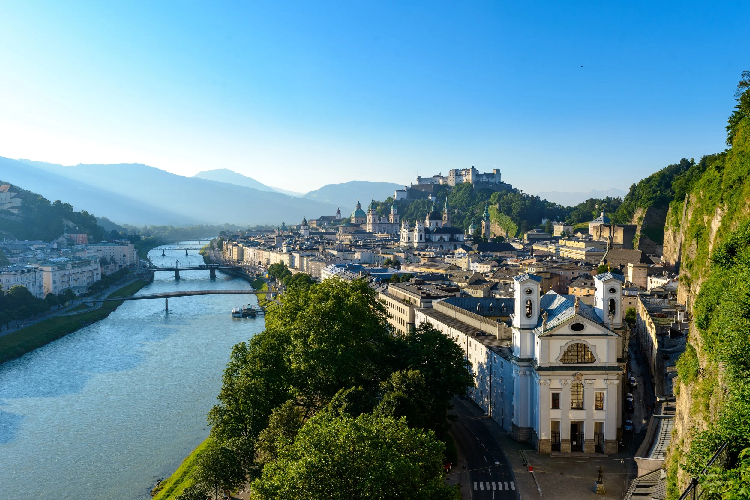 Salzburg mit Fluss mit Brücken im Vordergrund, historische Gebäude und grüne Hänge