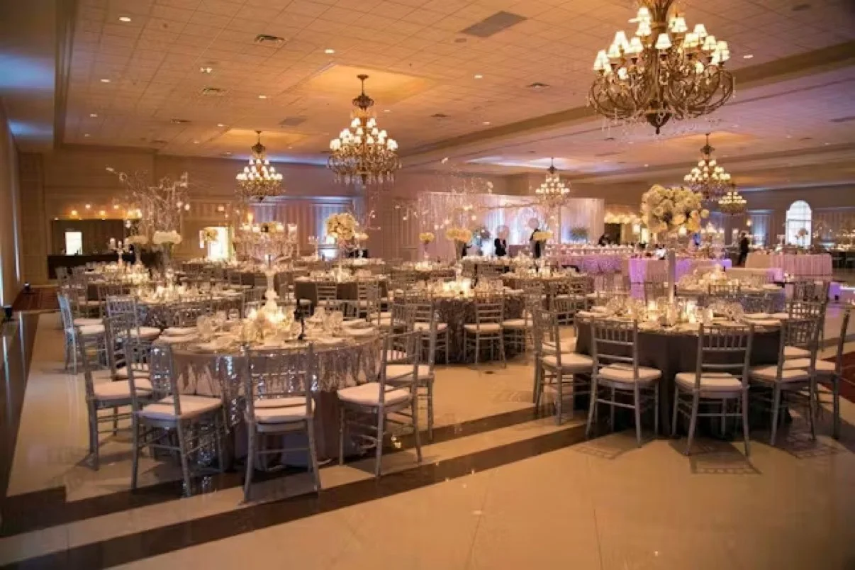 Chandelier-lit ballroom at the Palazzo Grande set for a wedding reception with round tables and tall floral centerpieces