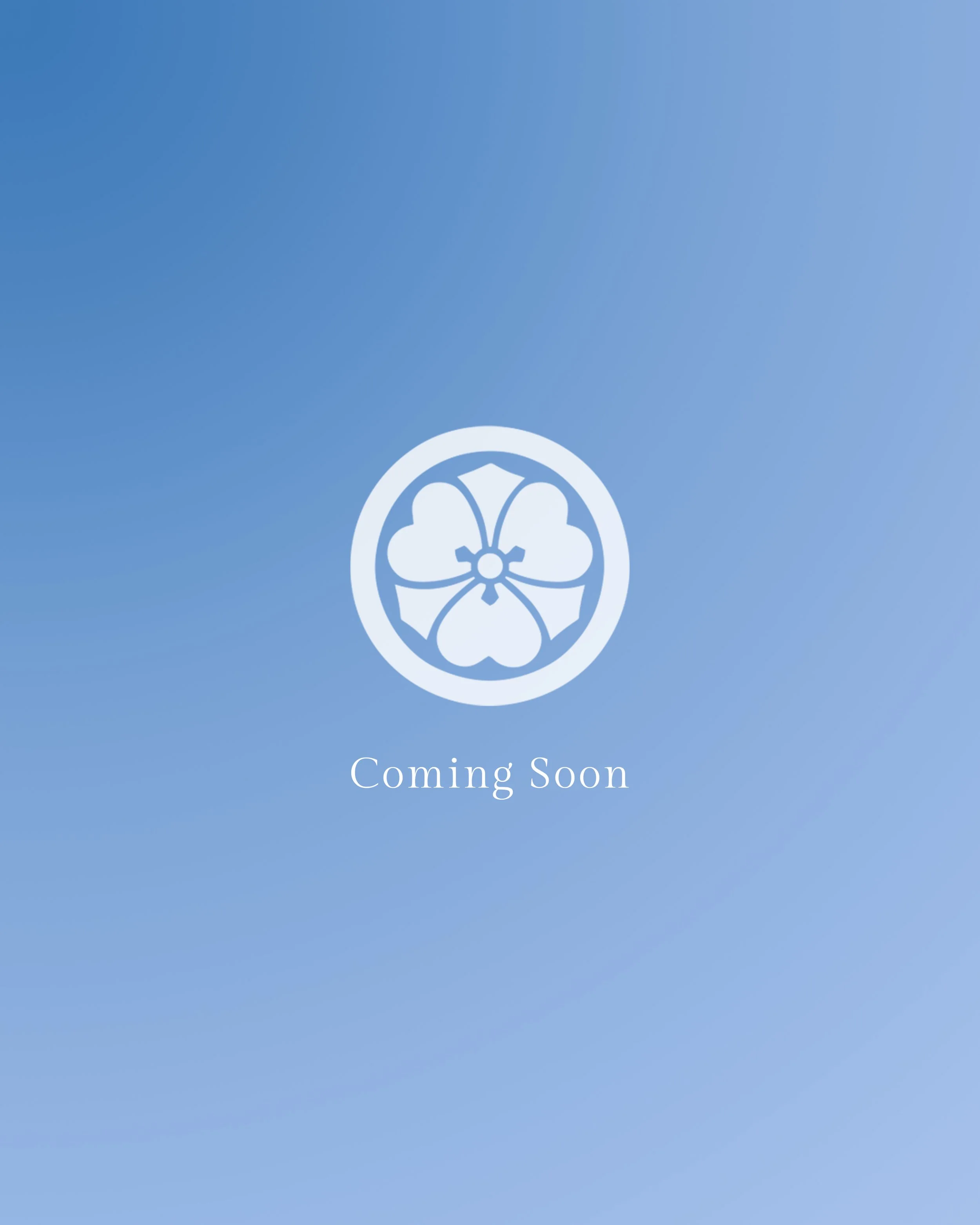 A blue gradient background with a white floral emblem at the bottom center and the text 'Coming Soon' in white in the middle.