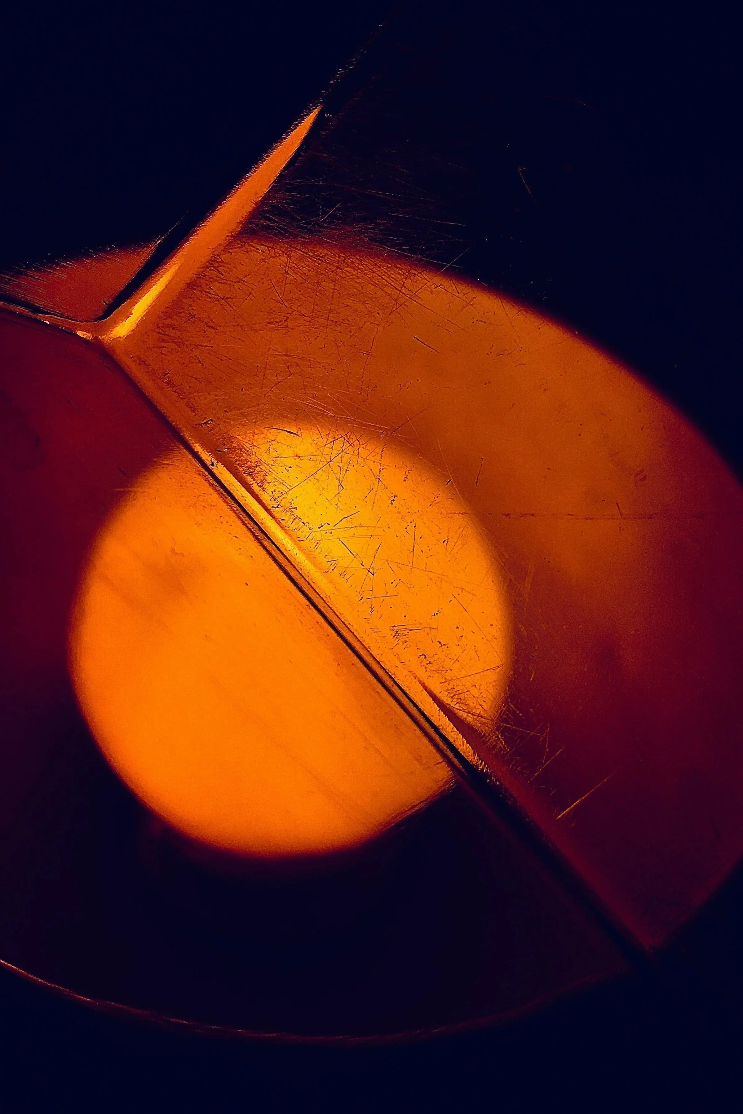 Close-up of a lit candle with an orange glow, surrounded by darkness.