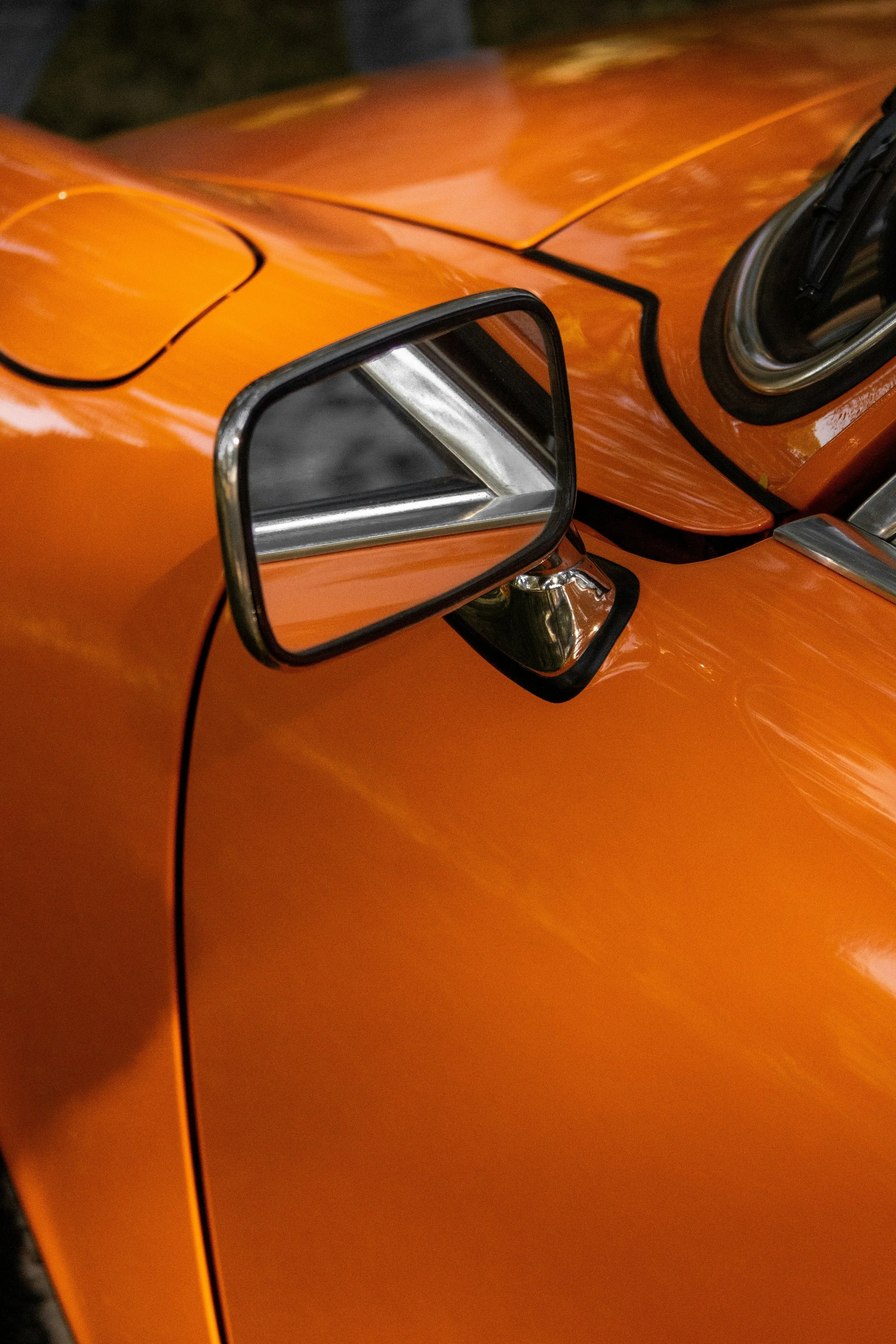 Close-up of an orange vintage car with a side mirror reflected on the door.