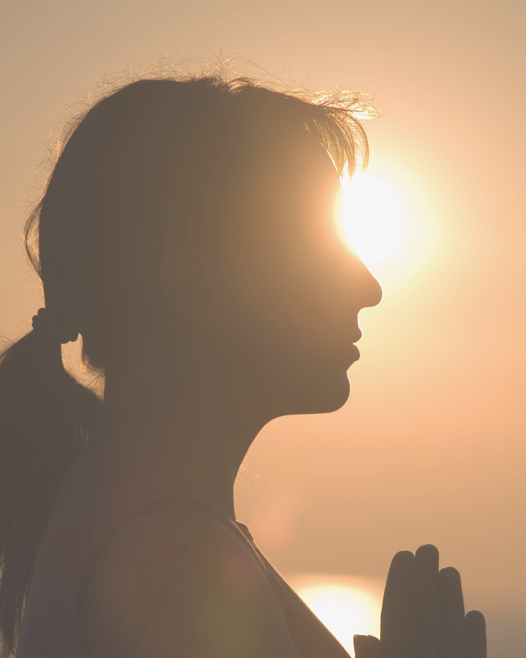 Silhouette of a woman with hands in meditation position at sunset.