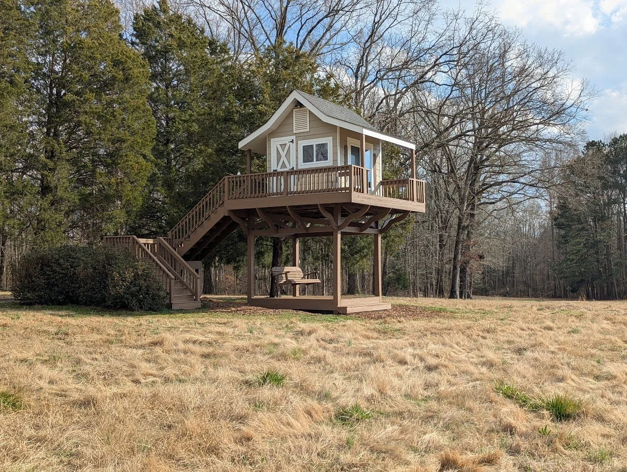 Wooden treehouse with a staircase and outdoor seating located on one of the Silent Retreat locations.