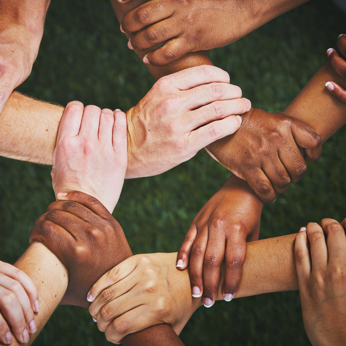 Multiple hands of various skin tones stacked on top of each other in a circle, symbolizing unity and diversity.