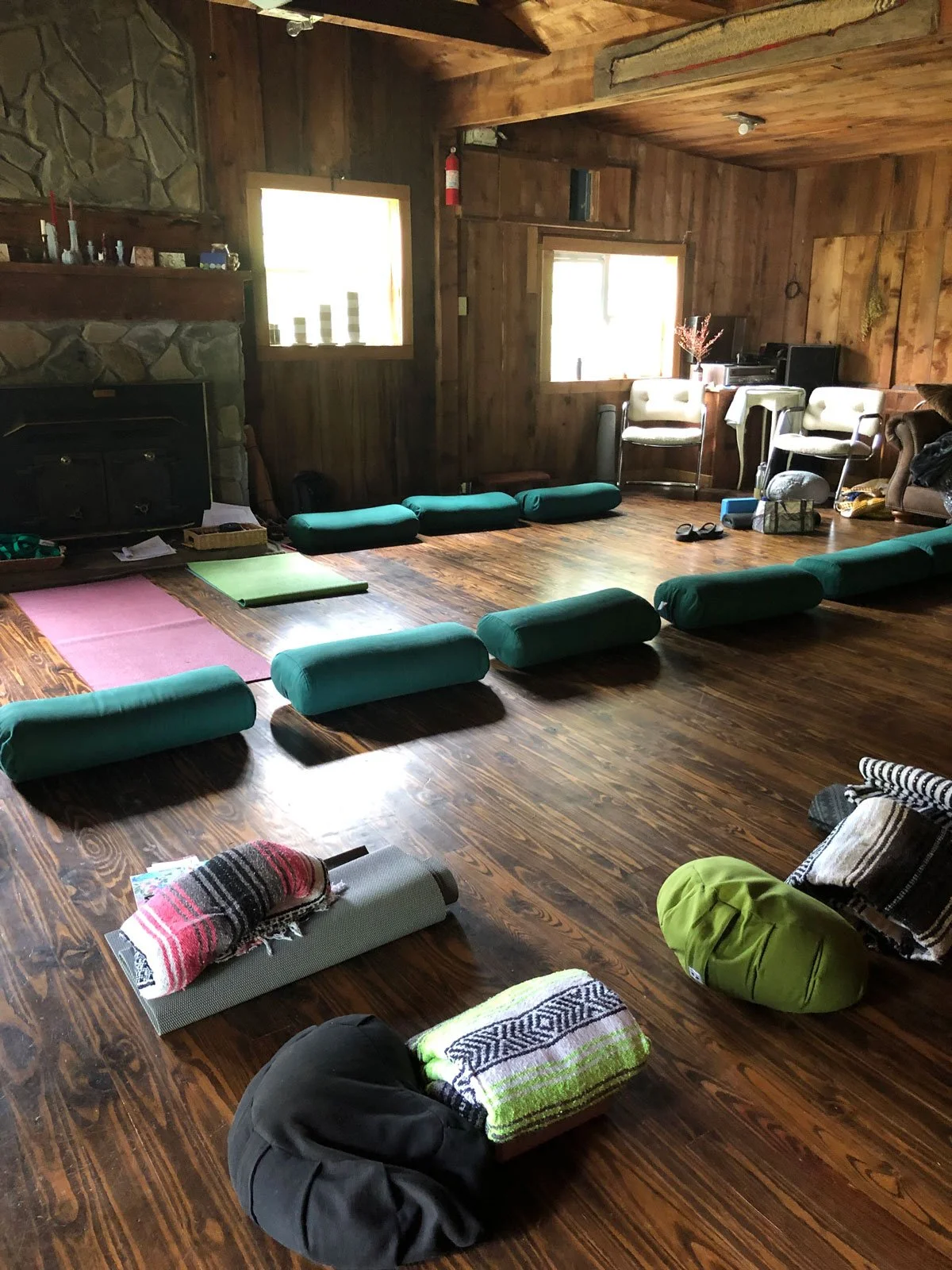 A wooden interior room set up for Silent Retreat with yoga mats, bolsters, blankets, and cushions.