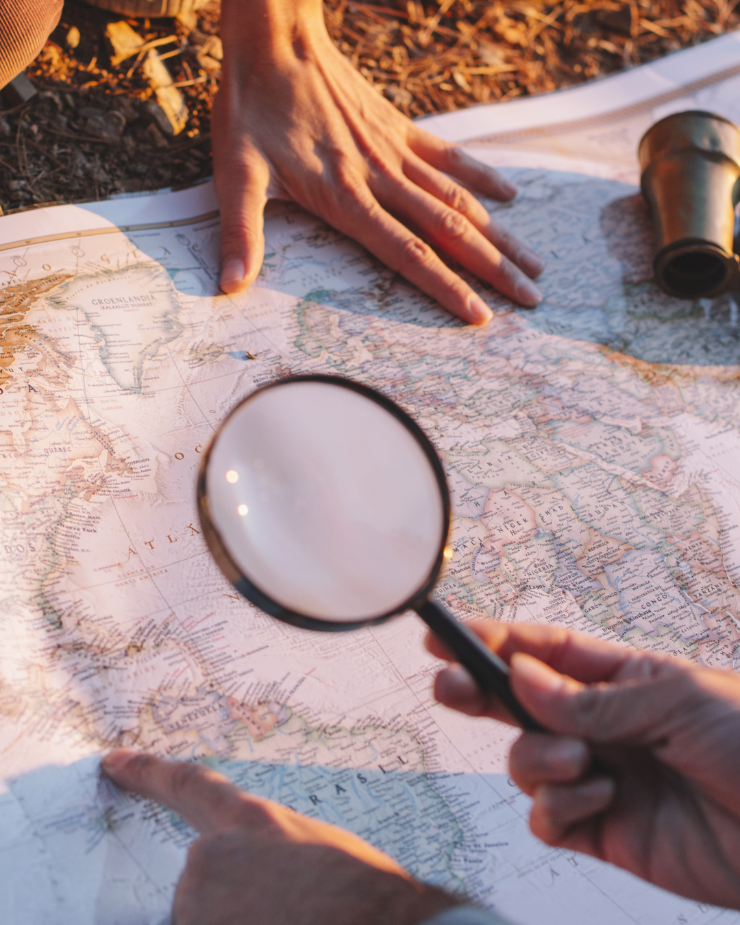 People examining a world map with a magnifying glass and binoculars