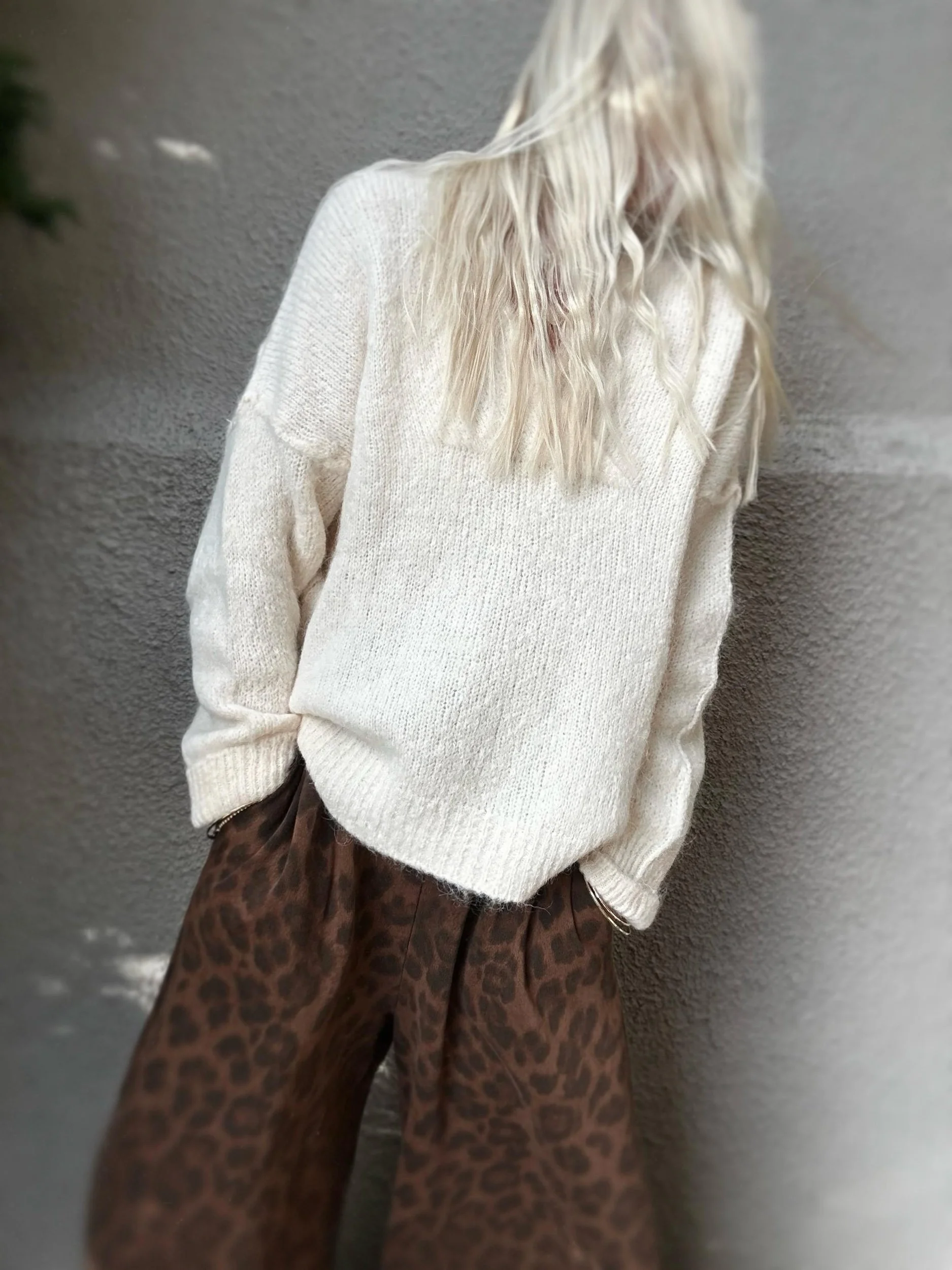 Woman wearing the cream Banditas Kula V-Neck Sweater with patterned brown pants, showing its loose fit and ribbed hem