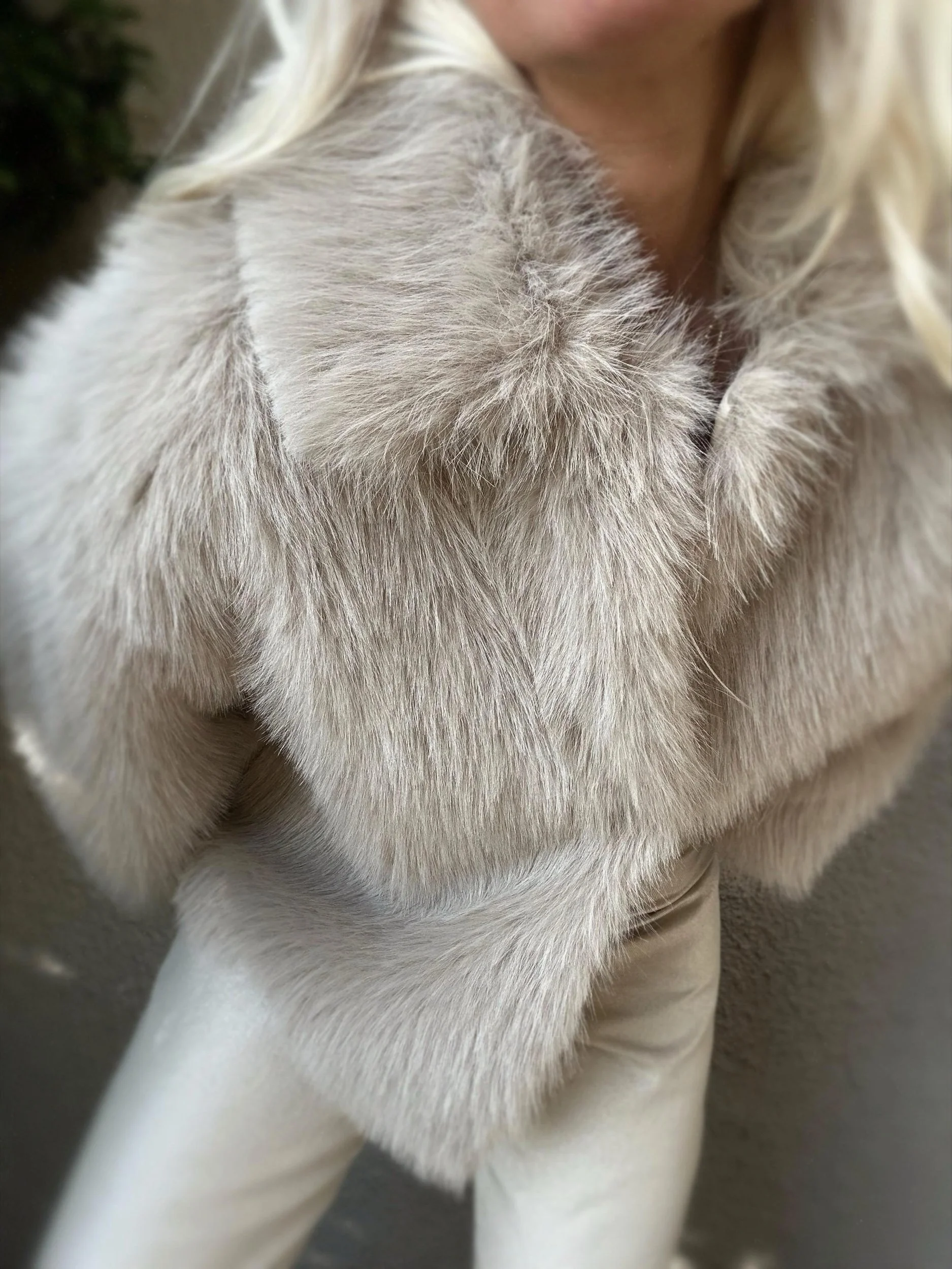 Woman wearing the cream Banditas Makena Faux Fur Jacket with oversized sleeves and light-colored pants