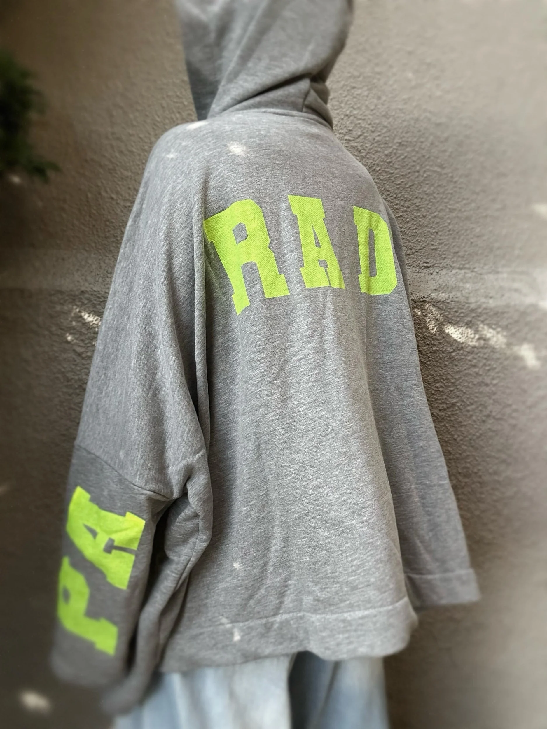 Close-up of neon green Paradise lettering on grey oversized sweatshirt